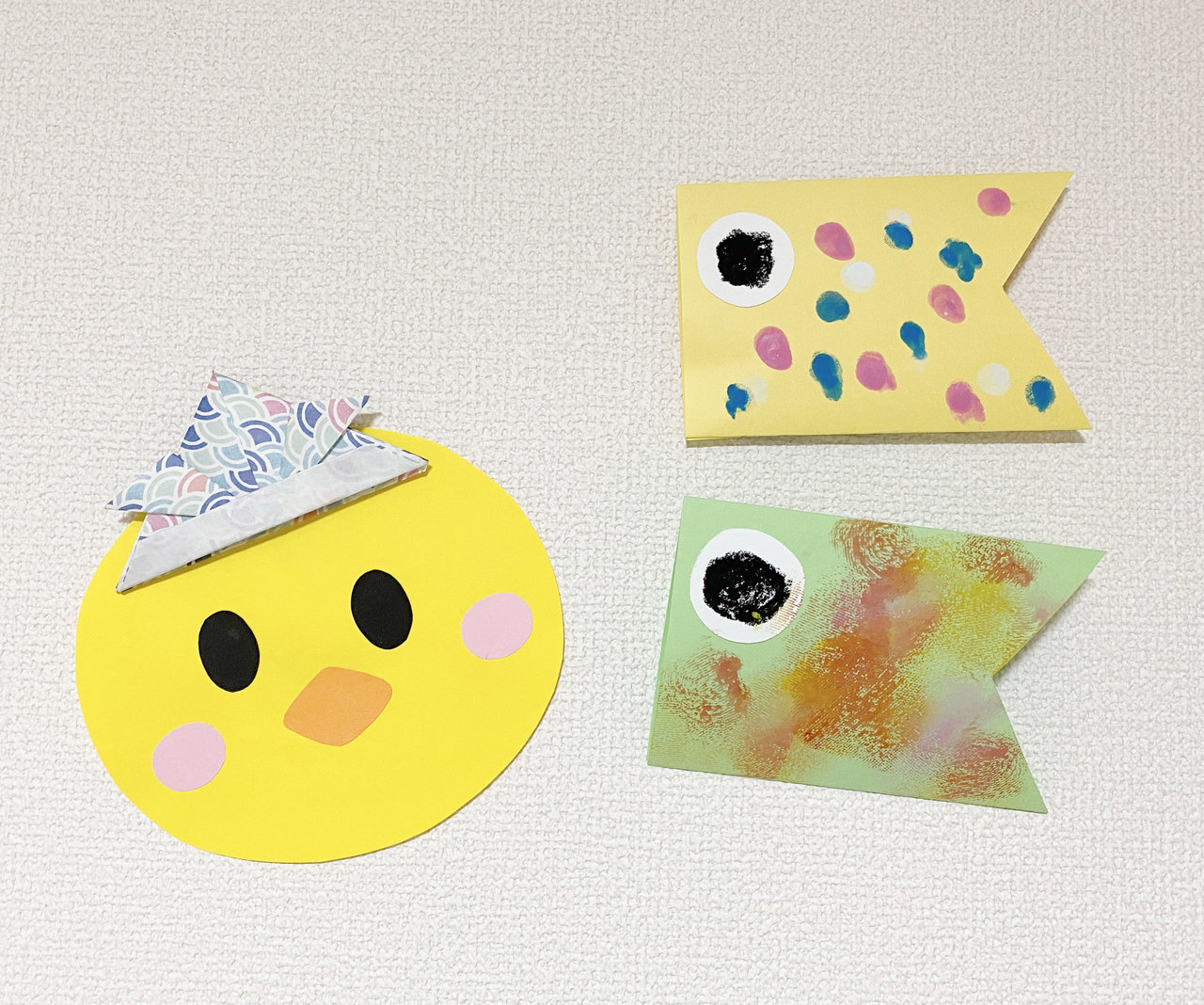 4月25日 土こいのぼり製作 各クラスのこいのぼり飾りを紹介します。0歳児ひよこ組は、小さな小さなかわいい足形をうろこに見立てました。3歳児 ぱんだ組はのりとクレヨンという、慣れてきた道具を使って画用紙にこいのぼりを飾りました。4歳児きりん組ははさみも使用し